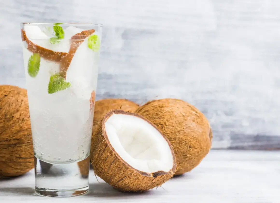 Orzeźwiający drink z wodą kokosową, lodem i miętą, obok świeżych kokosów. Idealny na upalne dni.