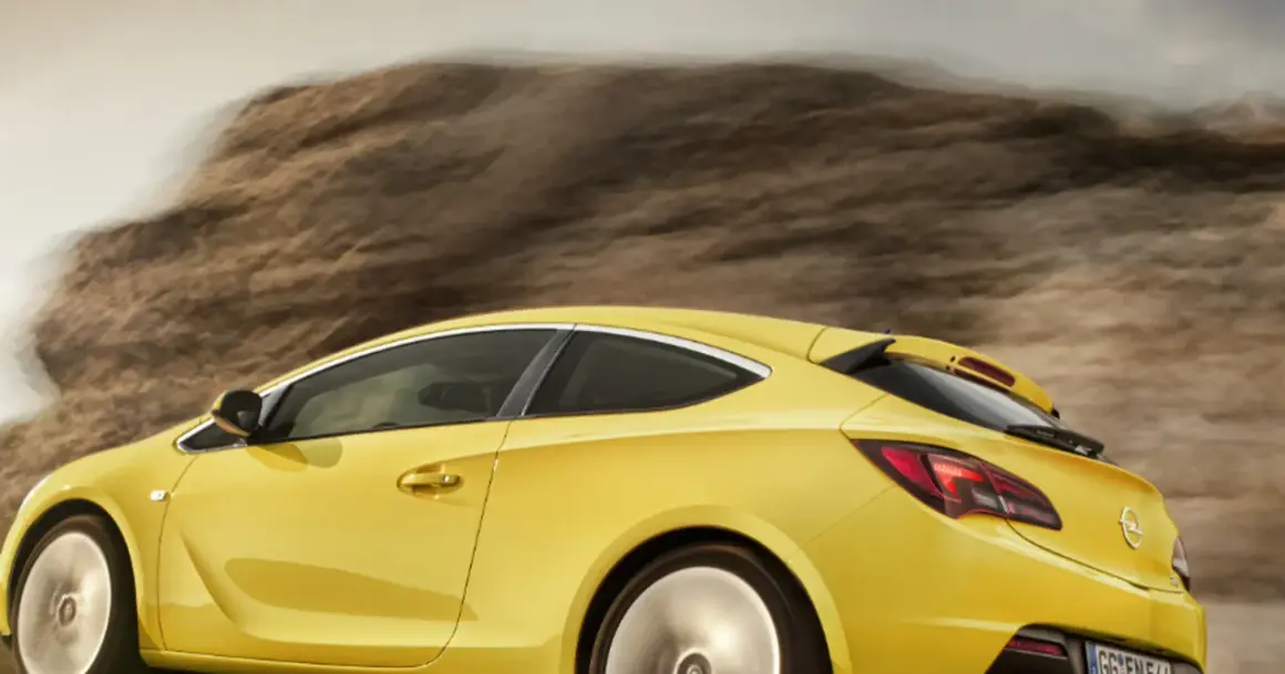 Żółty Opel Astra GTC pędzi przez pustynny krajobraz, zostawiając za sobą smugę kurzu.
