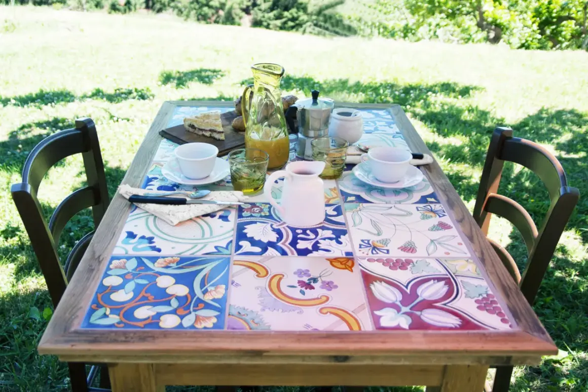 Tavolo con piastrelle fai da te, perfetto per un brunch all'aperto. Colori vivaci e motivi floreali creano un'atmosfera allegra.