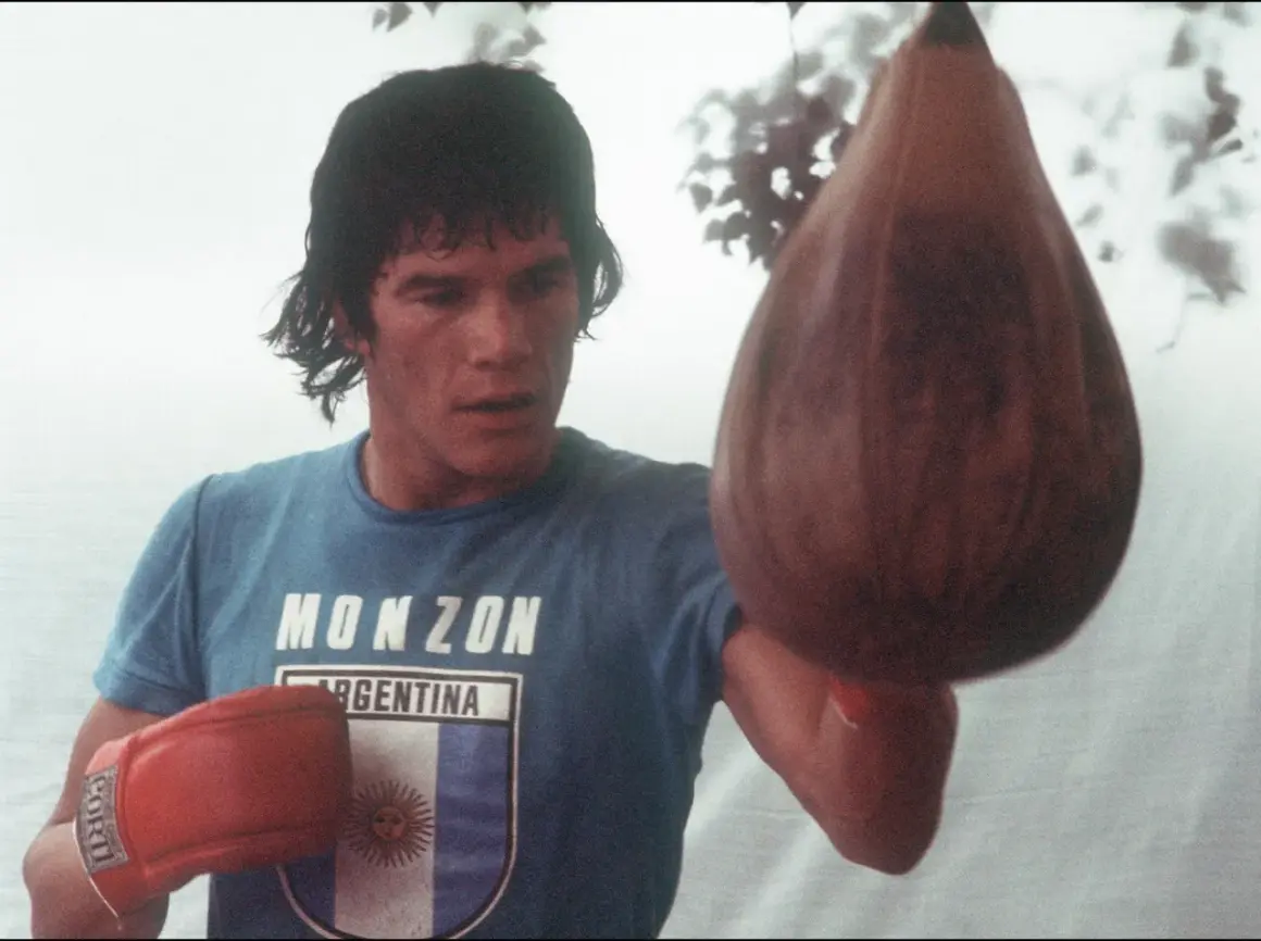 Carlos Monzón, the legendary boxer, trains with a speed bag, his blue shirt bearing his name and the Argentine flag.