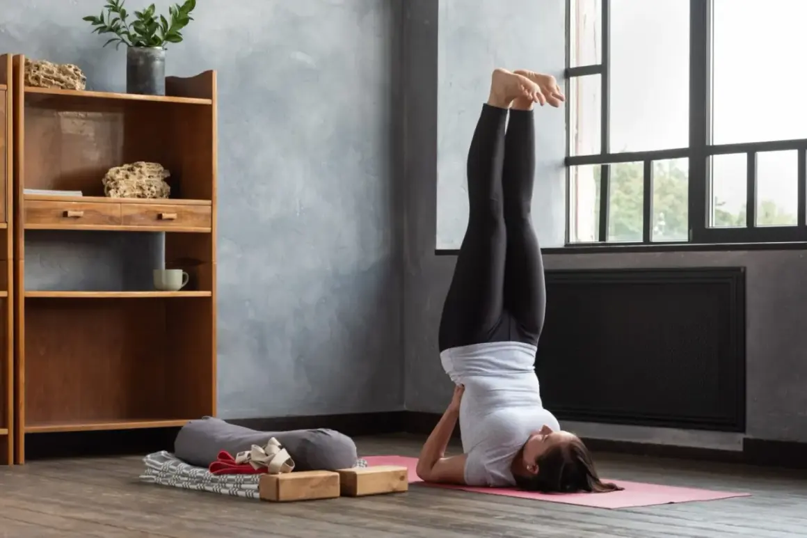 Frau praktiziert Iyengar Yoga in der Umkehrhaltung (Sarvangasana) auf einer rosa Matte, unterstützt von Holzblöcken.
