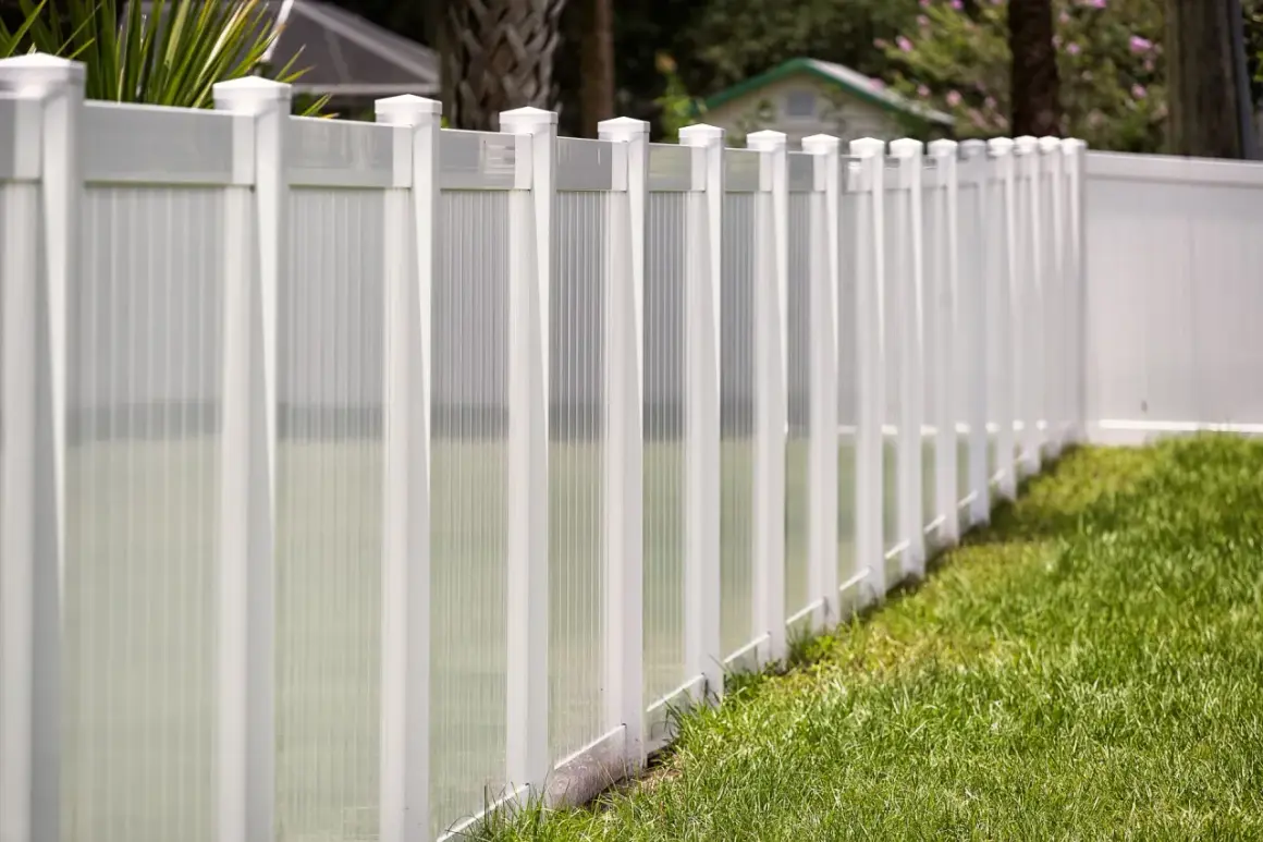A newly completed vinyl fence installation, featuring white posts and translucent panels, lines a lush green lawn.
