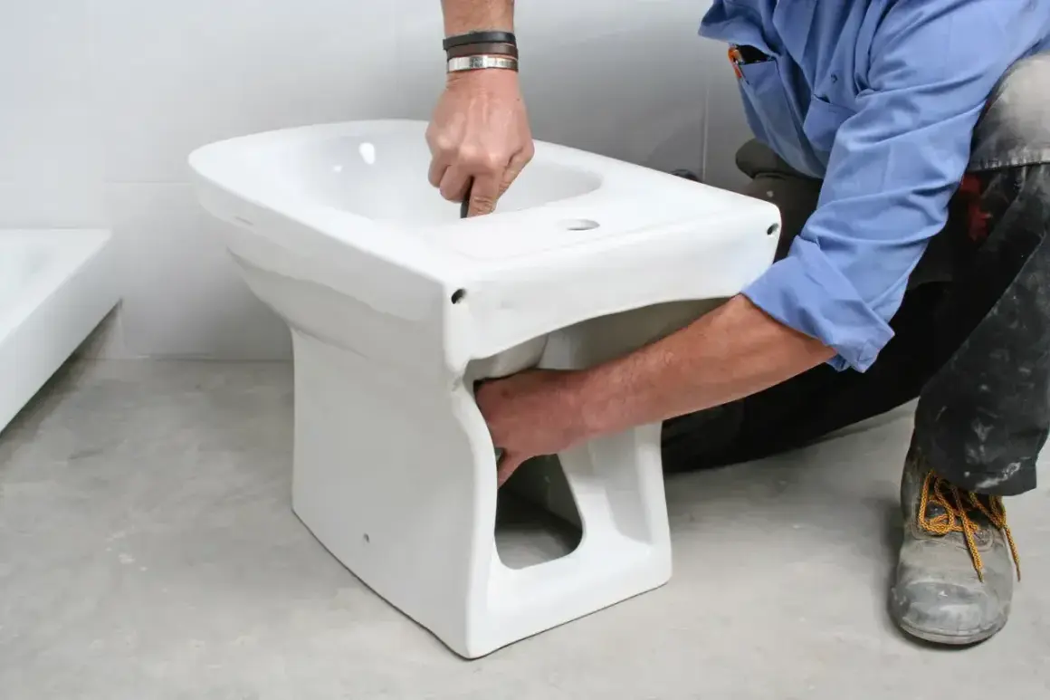 Instalator montuje białą ceramikę, pokazując, jak podłączyć bidet.