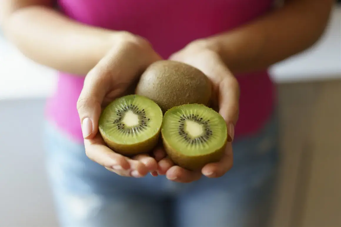 Dłonie trzymają całe i przekrojone kiwi. Ten owoc to naturalny sposób na zaparcia.