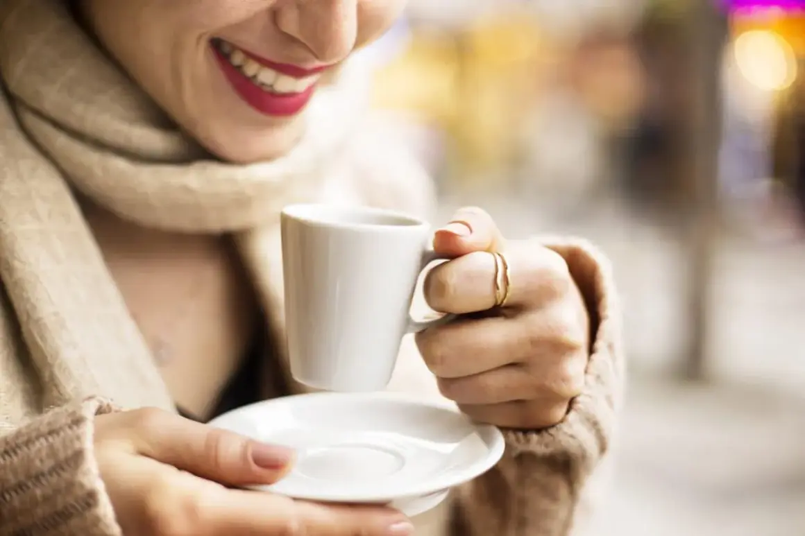 Donna sorride tenendo una tazzina di caffè. Speriamo non sia troppo acquoso, come a volte capita con la macchina del caffè.