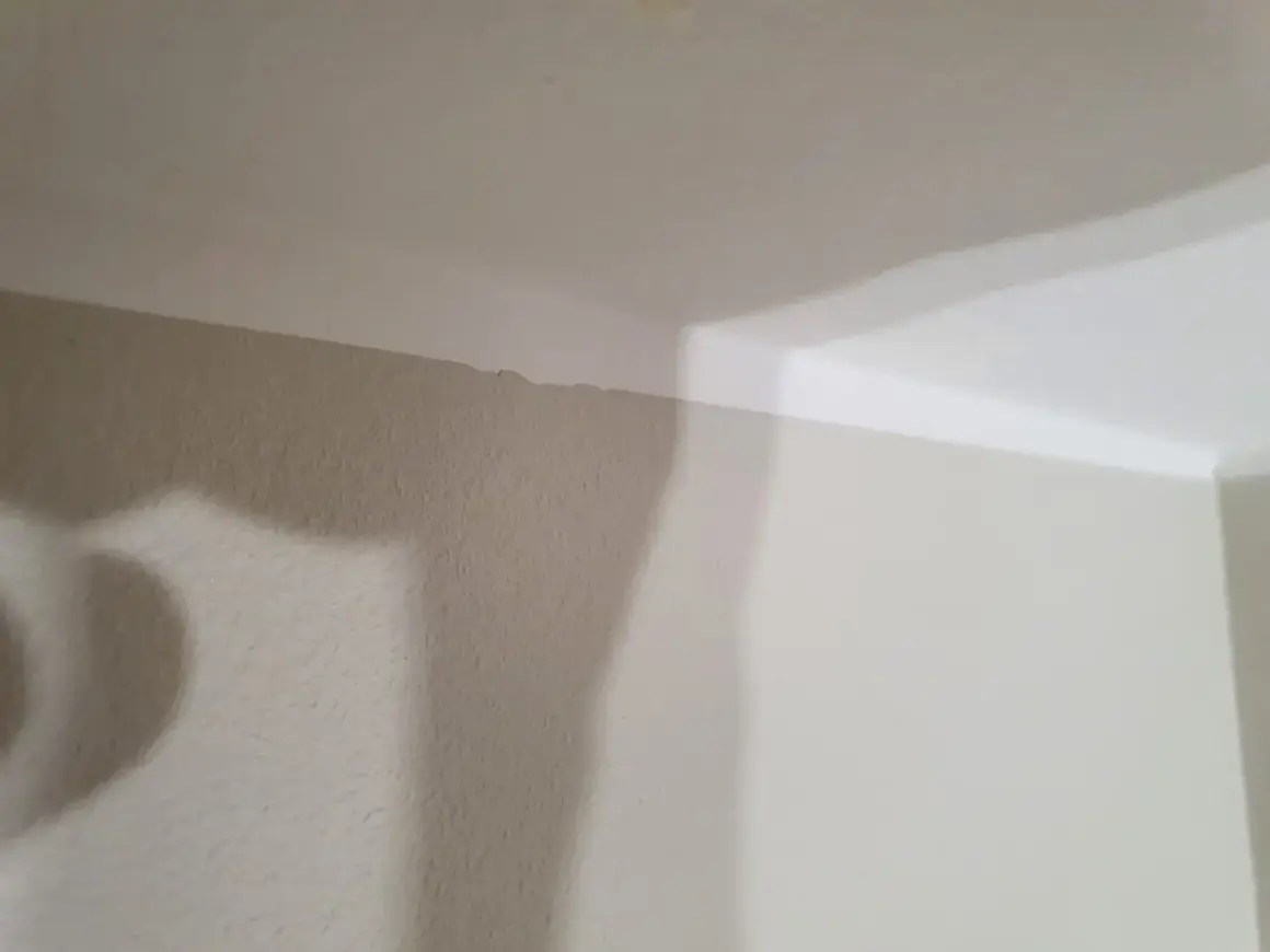 En snedtakad vägg med en ojämn kant där taket möter väggen. En skugga faller över väggen.