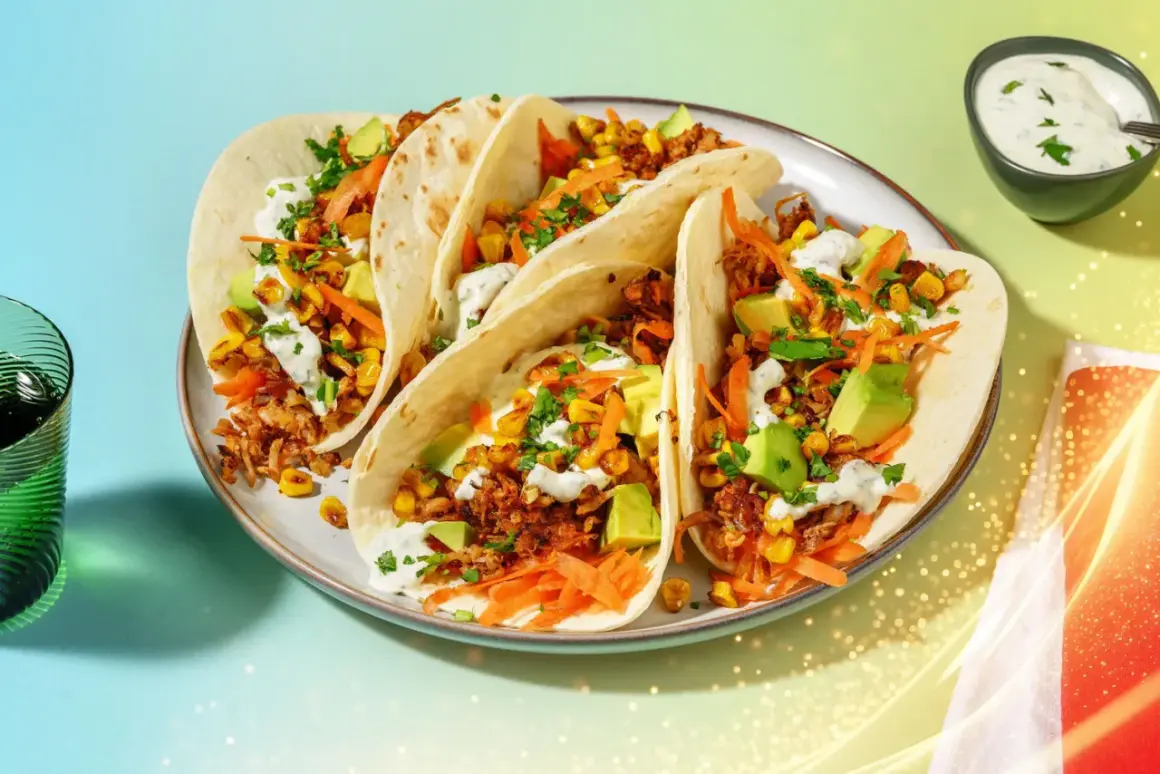 Här är en tallrik med pulled pork tacos, fyllda med majs, avokado och strimlad morot, toppade med en krämig sås.