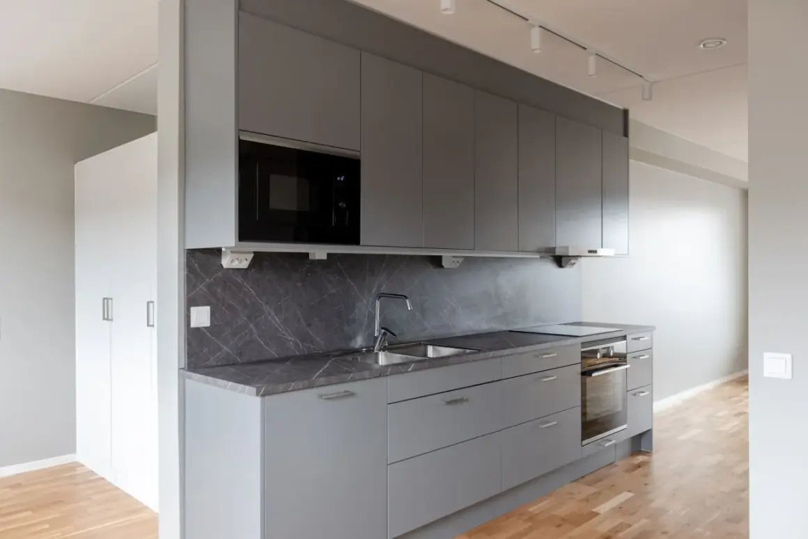 Modernt kök med grå skåp, mörk bänkskiva och integrerad mikrovågsugn. Ett stilrent Bålsta apartment hotel.