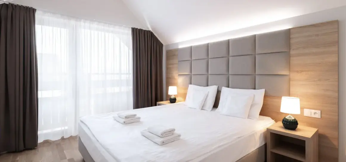 Przytulna sypialnia z dużym łóżkiem, miękkim zagłówkiem i zasłonami. "Room only" to oferta noclegu bez wyżywienia.