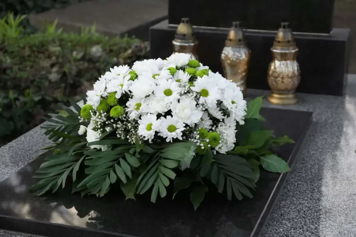 Piękne wiązanki ze sztucznych kwiatów, białe chryzantemy i zielone kulki, ozdabiają nagrobek.
