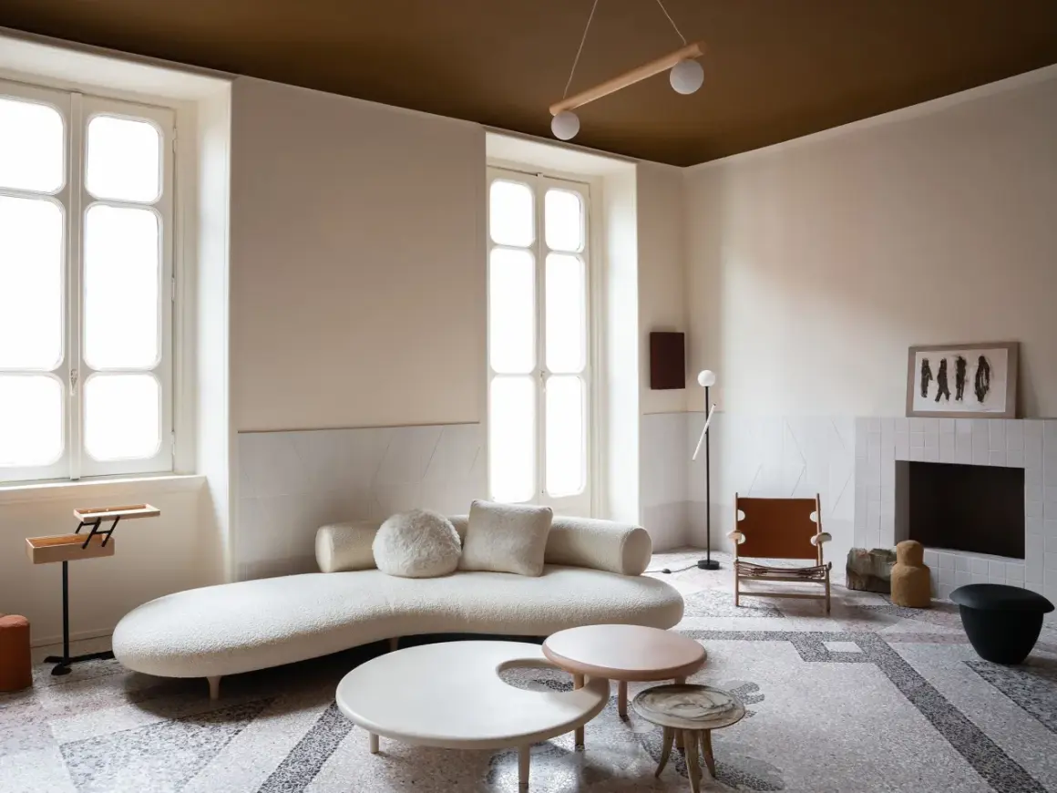 Salotto moderno con divano curvo, tavolini dalle forme organiche e un camino. Le pareti e il soffitto stesso colore creano un'atmosfera avvolgente.