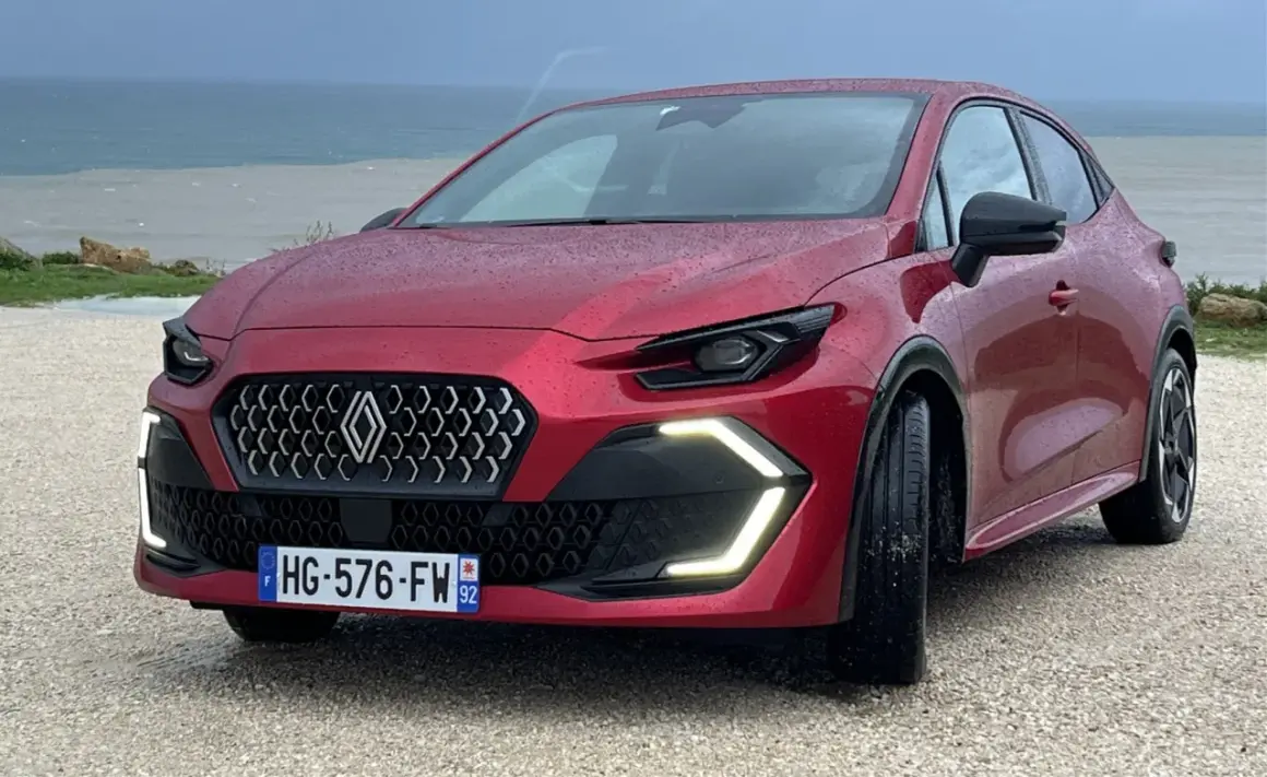Nowe Clio 2026 w kolorze czerwonym, z nowoczesnym grillem i światłami LED, zaparkowane nad morzem.