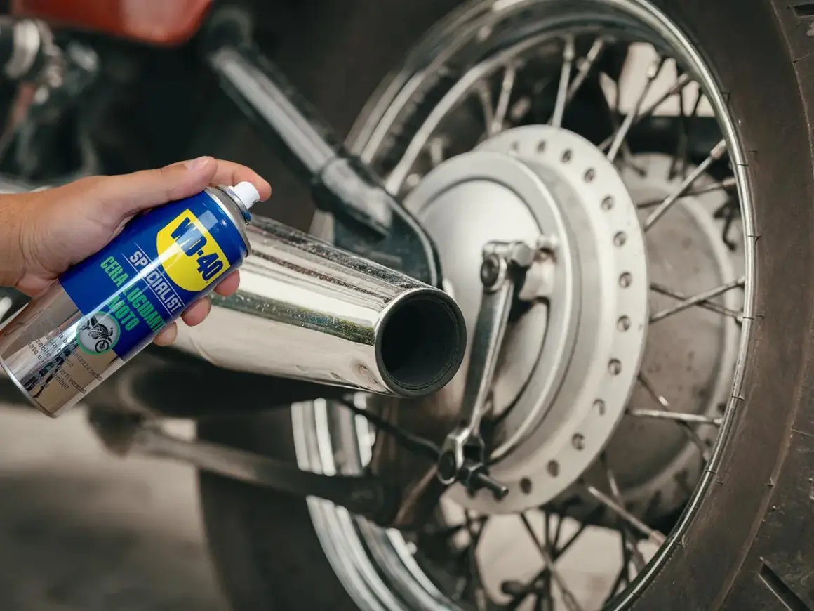 Mano che spruzza cera lucidante WD-40 su uno scarico cromato per lucidare la moto.