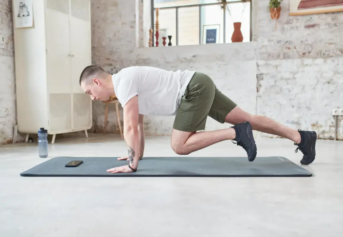 Un homme en short vert effectue un exercice de gainage latéral sur un tapis de yoga.
