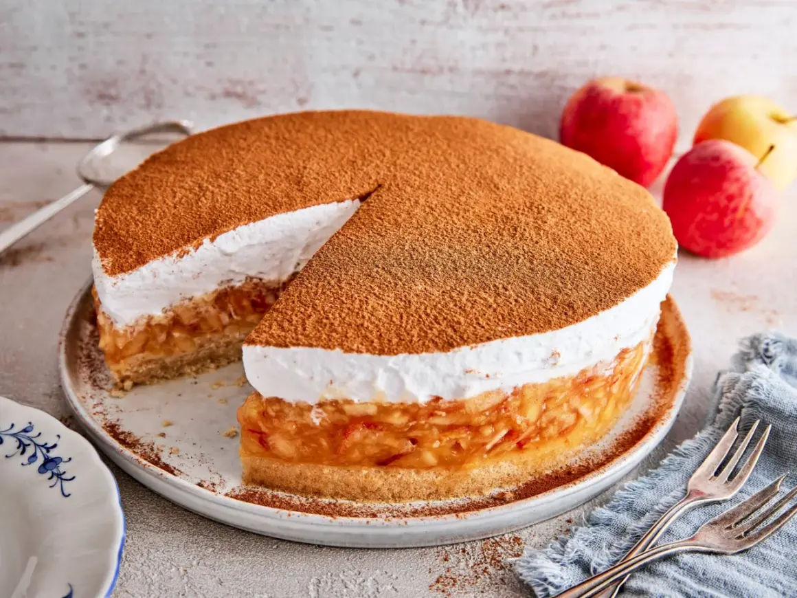 Eine köstliche schwedische Apfeltorte mit einer luftigen Sahnehaube, bestäubt mit Zimt. Daneben liegen frische Äpfel.