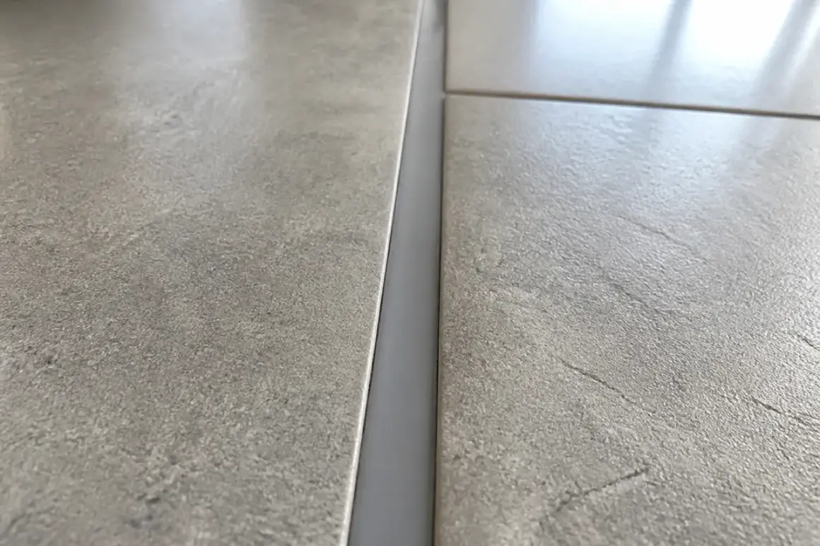 Gros plan sur un joint de dilatation carrelage gris, entre deux carreaux texturés.