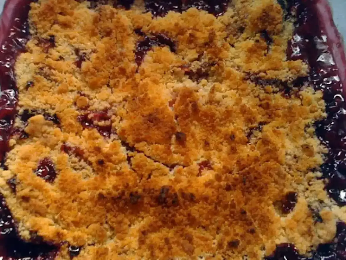 Delicioso crumble de ciruelas recién horneado, con una capa dorada y crujiente sobre la fruta jugosa.
