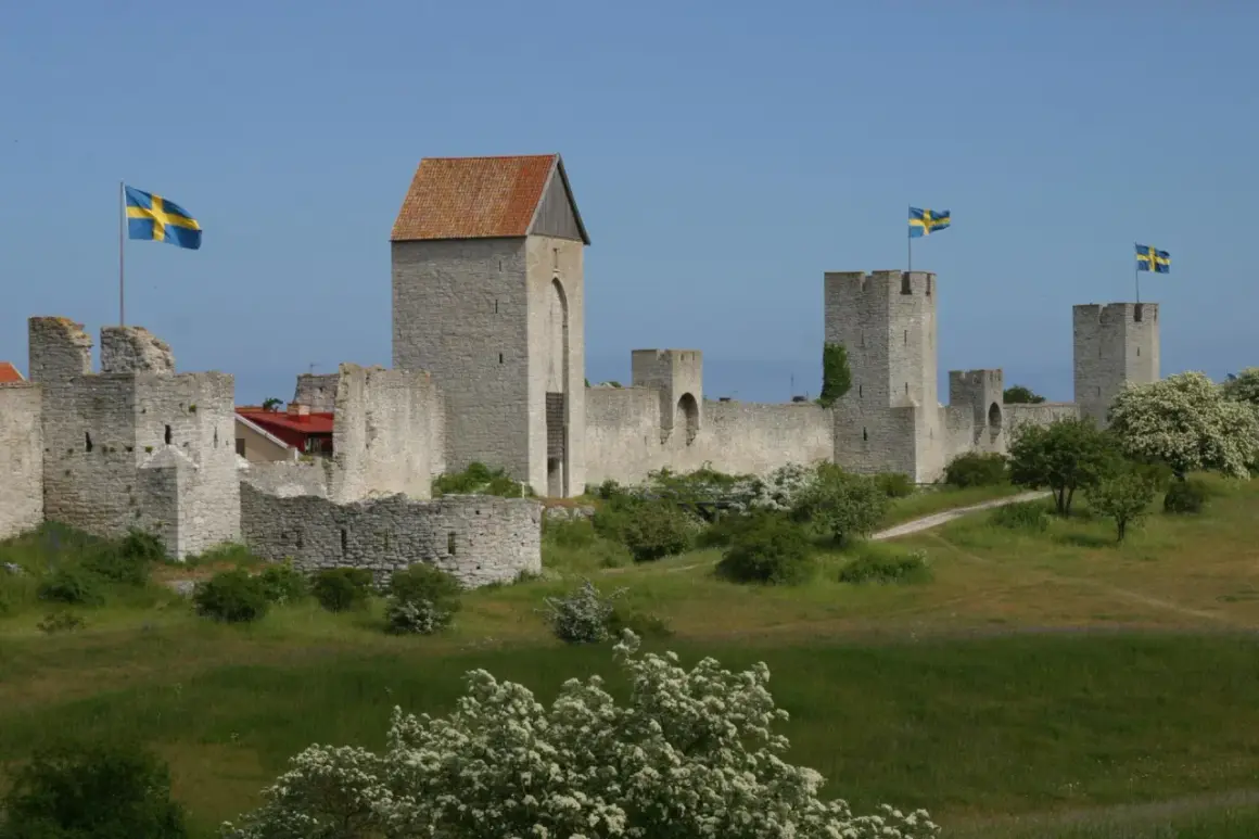 Visby muren reser sig stolt mot en blå himmel, med svenska flaggor som vajar från tornen. En historisk stadsvall som vittnar om svunna tider.