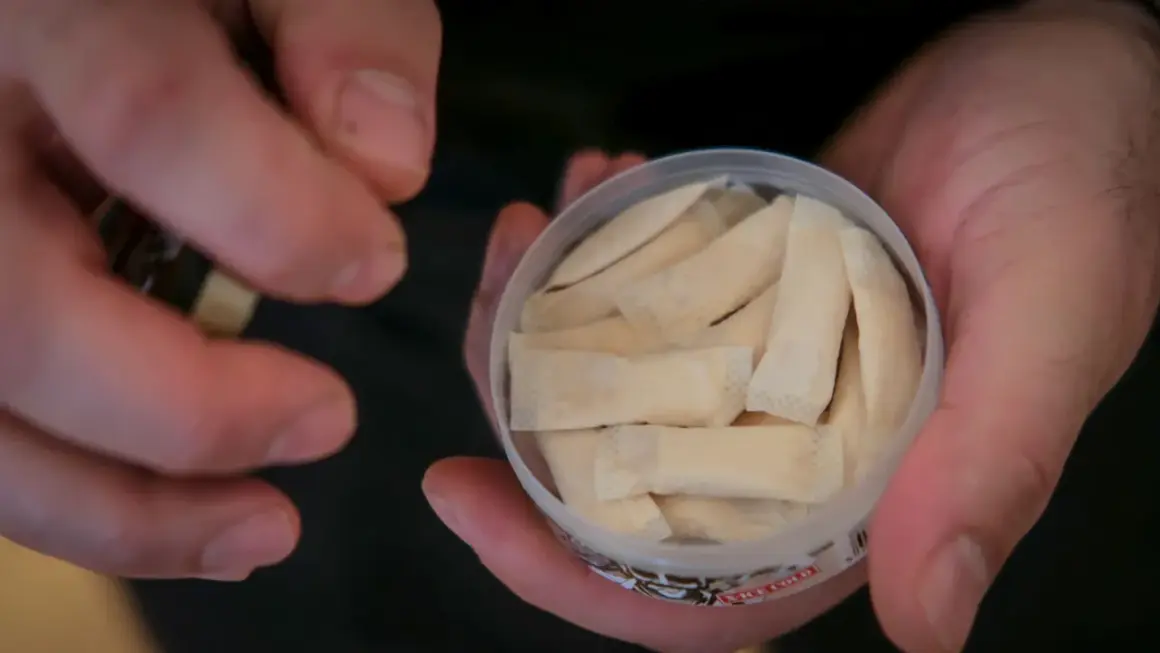 En hand håller en dosa med flera påsar. Det ser ut som fake snus, men det är svårt att säga säkert.