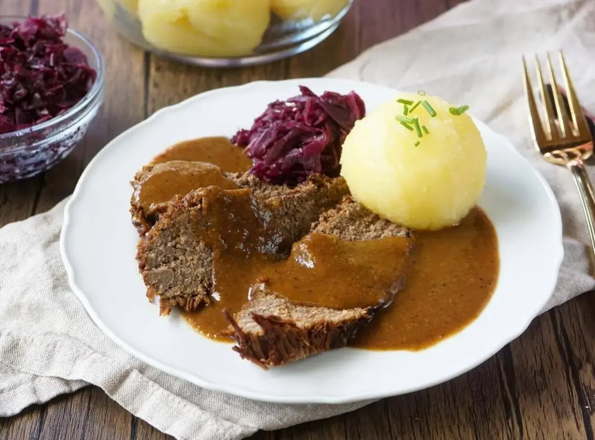Sauerbraten rezept: Zarte Scheiben Braten in dunkler Sauce, serviert mit Rotkohl und Klößen. Ein Klassiker der deutschen Küche.