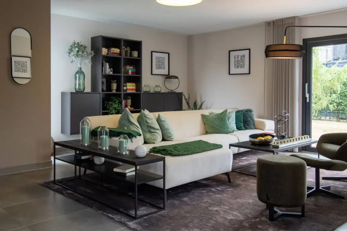 Modernes Wohnzimmer mit beigem Sofa, grünen Akzenten und hellgrauen Wänden. Diese Wandfarben sind modern und schaffen eine ruhige Atmosphäre.