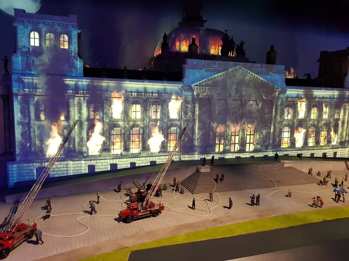 Miniaturowy pożar Reichstagu w **little big city Berlin**. Strażacy walczą z płomieniami, a dym unosi się w mroku.