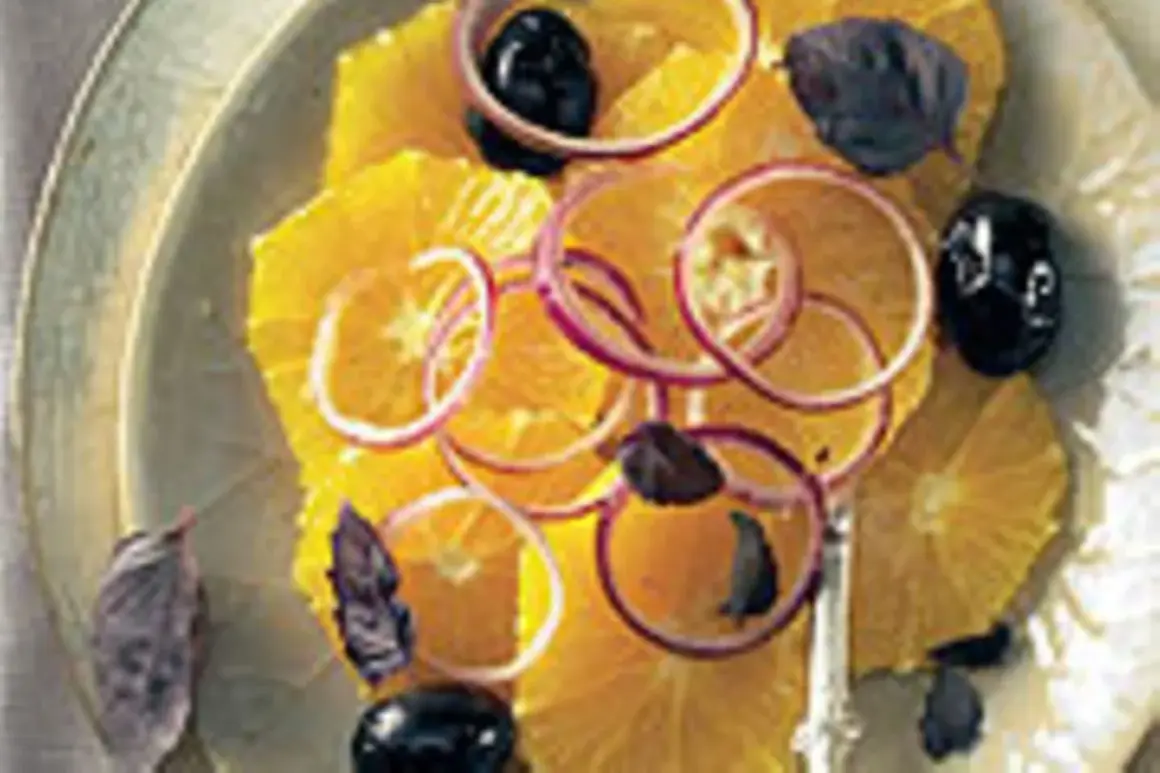 Erfrischender Salat mit Orangen, roten Zwiebelringen, schwarzen Oliven und dunklen Kräutern auf einem Teller.