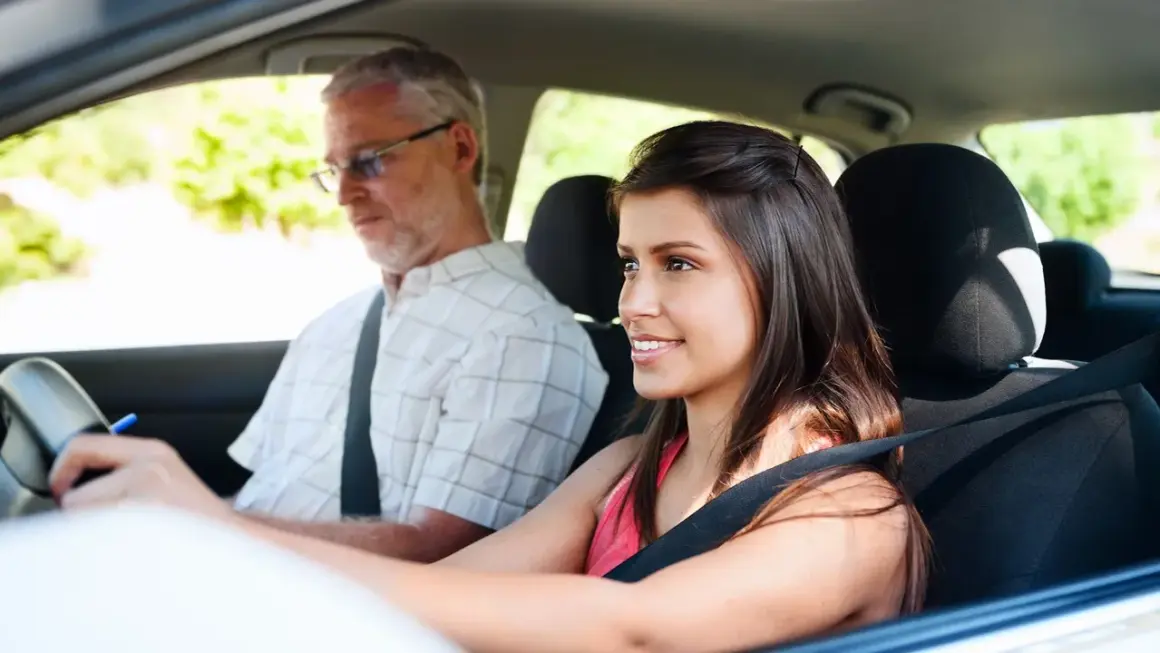 Une jeune femme souriante apprend à conduire avec un homme plus âgé, profitant de la nouvelle loi sur le permis à 16 ans.