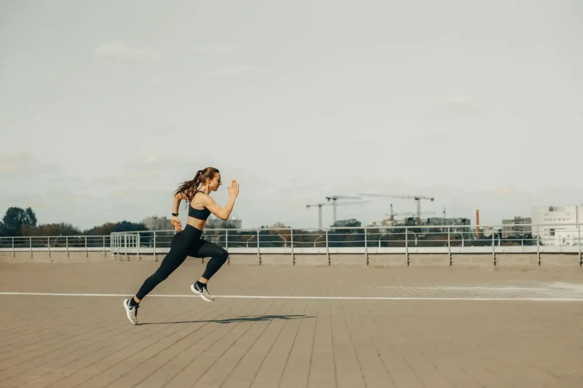 Kobieta w sportowym stroju biegnie, pokonując dystans 5 km. W tle widać miejską panoramę z dźwigami budowlanymi.