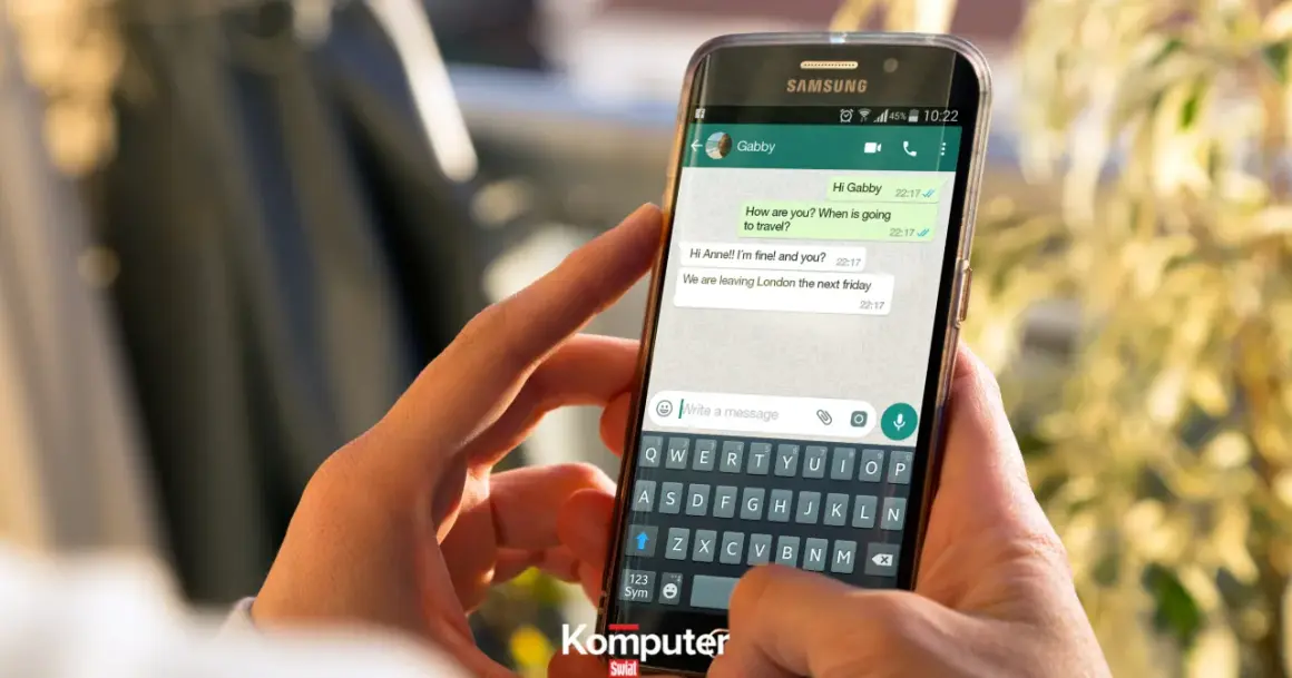 Dłonie trzymające smartfon z otwartym WhatsAppem. Widoczna klawiatura i okno czatu, jak założyć WhatsAppa.