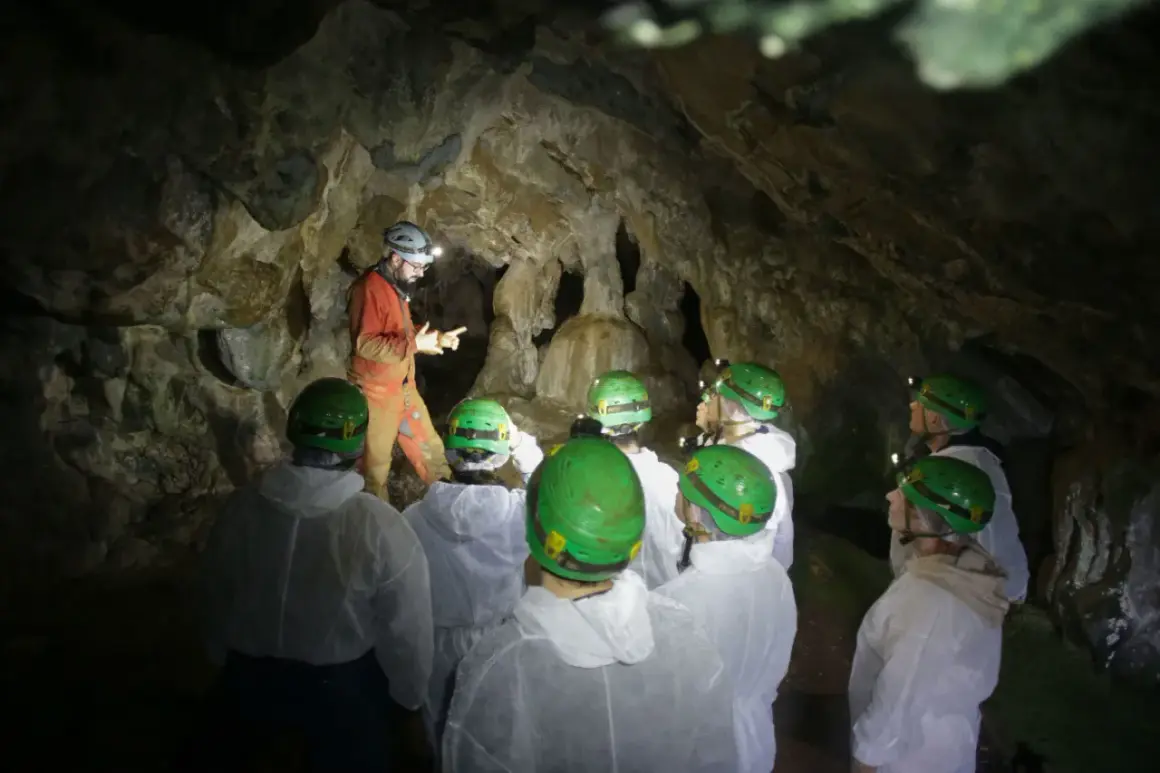 Exploradores en la cueva Rei Cintolo, con cascos verdes y trajes blancos, escuchan atentamente a su guía.