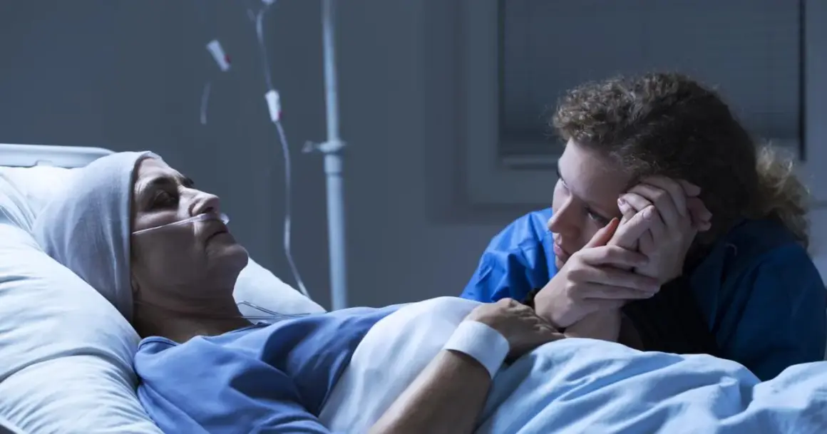 Chora kobieta w łóżku szpitalnym, podłączona do aparatury, trzyma za rękę bliską osobę. Czy leczenie paliatywne to koniec?