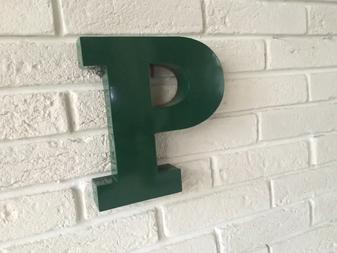 Une lettre murale verte en forme de P est fixée sur un mur de briques blanches.