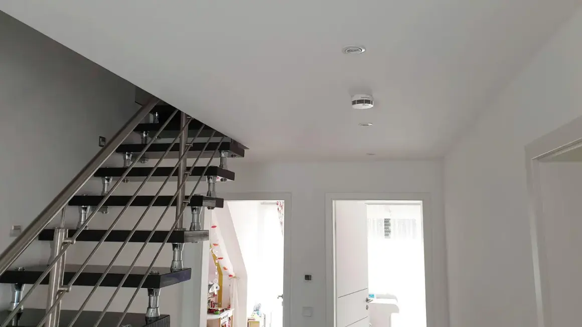 Moderner Flur mit Treppe und einem weißen rauchmelder an der Decke, der für Sicherheit sorgt.