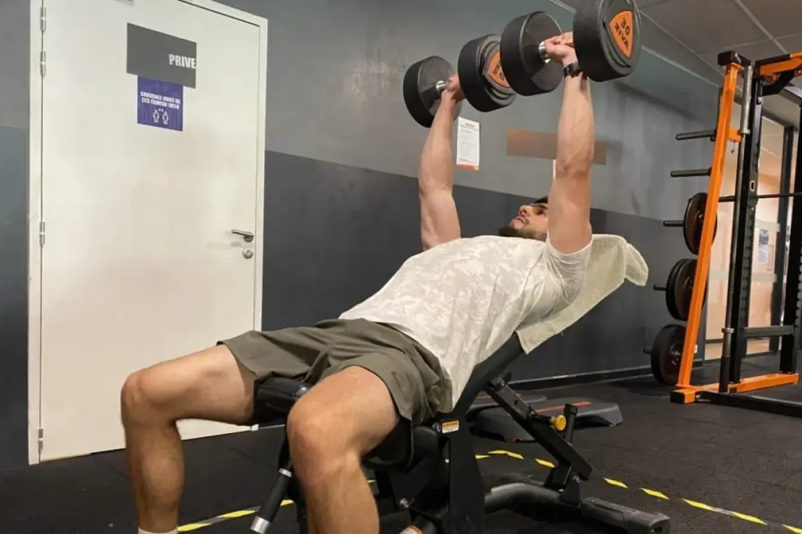 Un homme fait un exercice pectoraux avec des haltères sur un banc incliné dans une salle de sport.