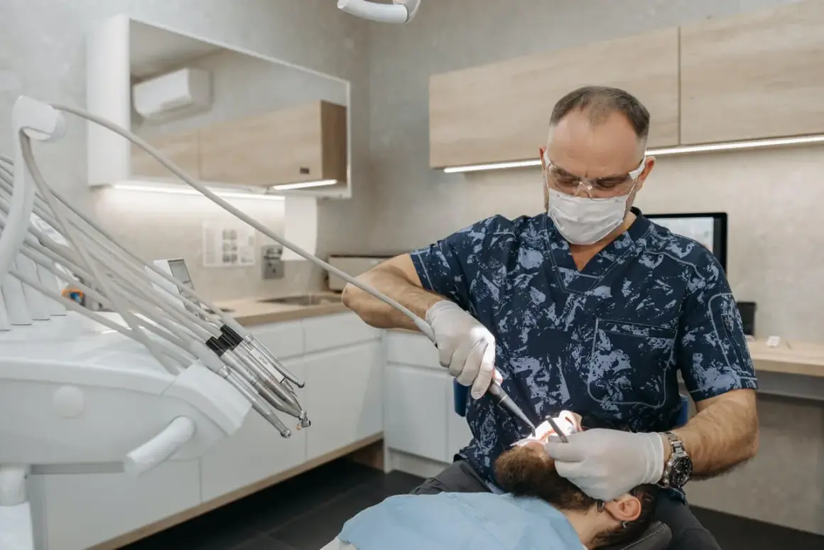 Dentysta w masce i okularach wykonuje zabieg, być może kortykotomię, u pacjenta leżącego na fotelu.