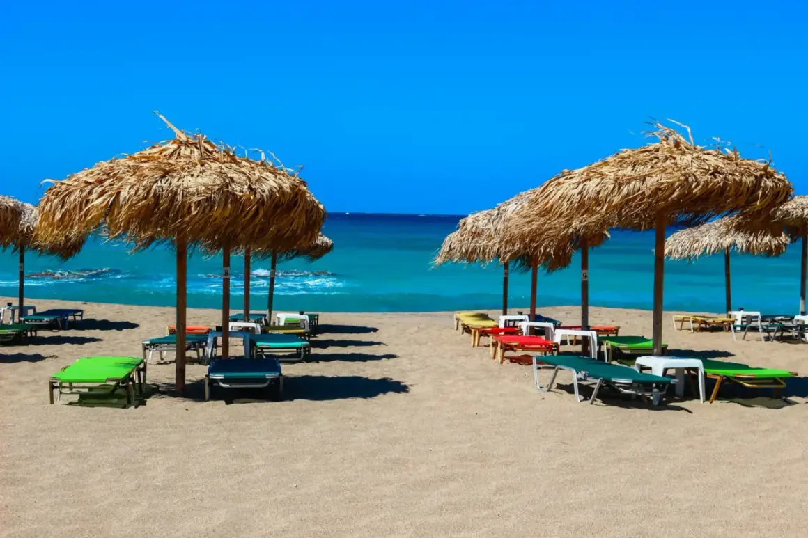 Słomiane parasole i leżaki na piaszczystej plaży Falasarna, z turkusowym morzem w tle.