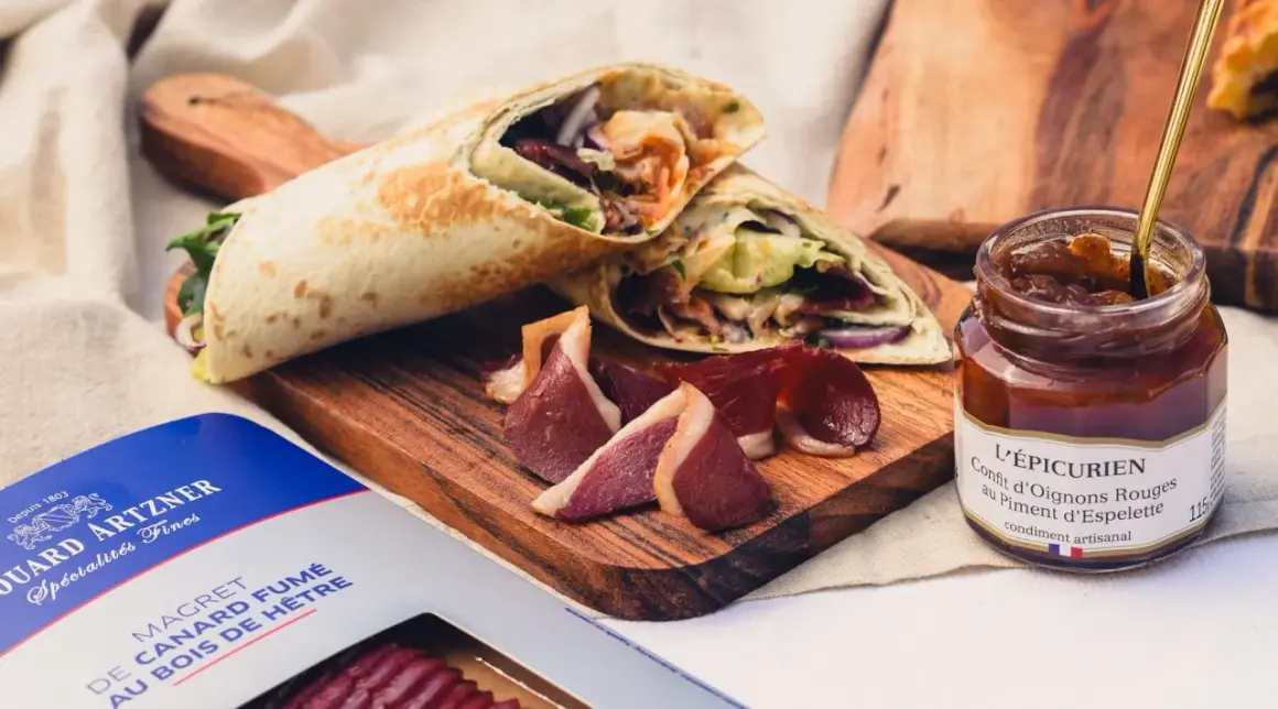 Wrap de magret de canard fumé, servi avec des tranches de canard et un confit d'oignons rouges.