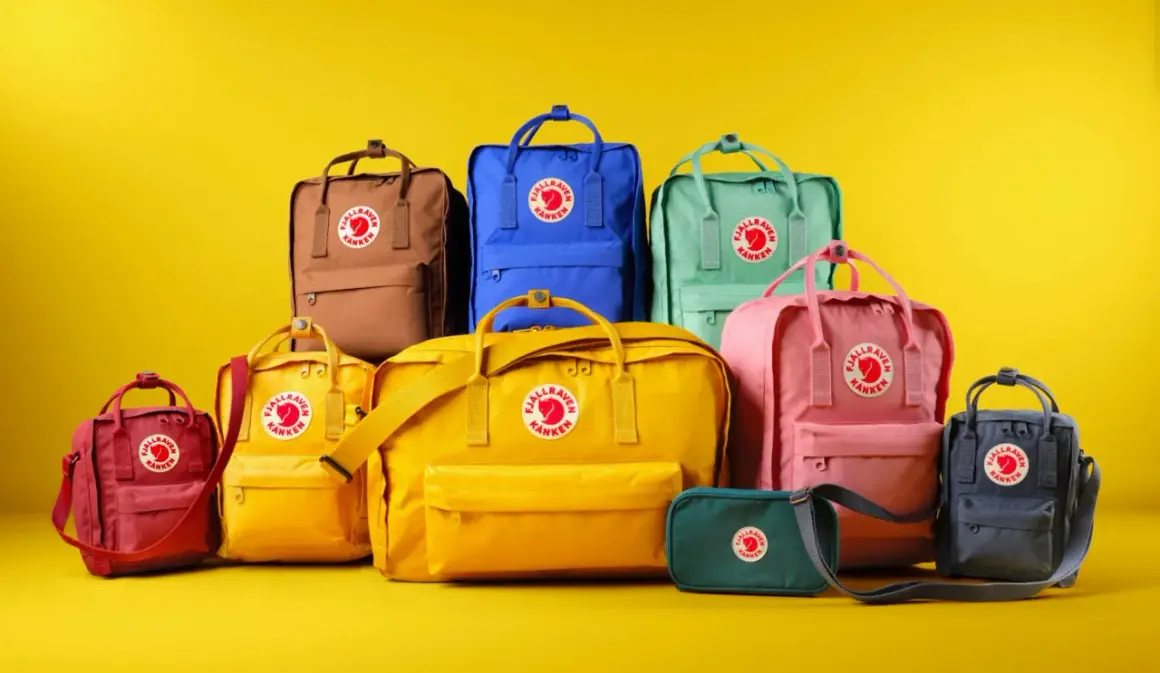 En samling färgglada Fjällräven Kånken-ryggsäckar i olika fjällräven ryggsäck storlek, från små till stora, mot en gul bakgrund.