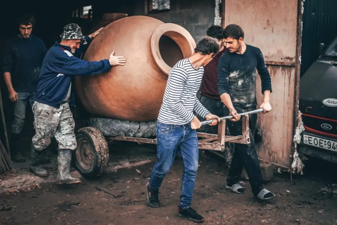Mężczyźni przenoszą wielką glinianą qvevri, tradycyjny gruziński pojemnik do produkcji win.