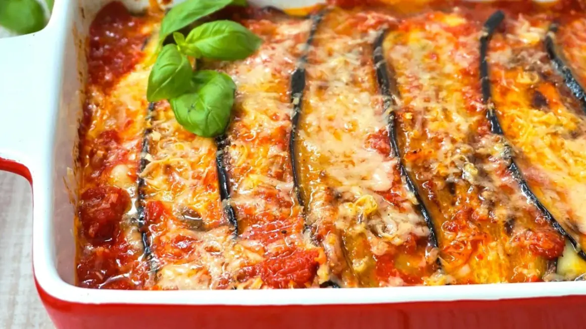 Berenjenas a la parmesana recién horneadas, burbujeantes y doradas, con queso fundido y un toque de albahaca fresca. ¡Un plato italiano irresistible!