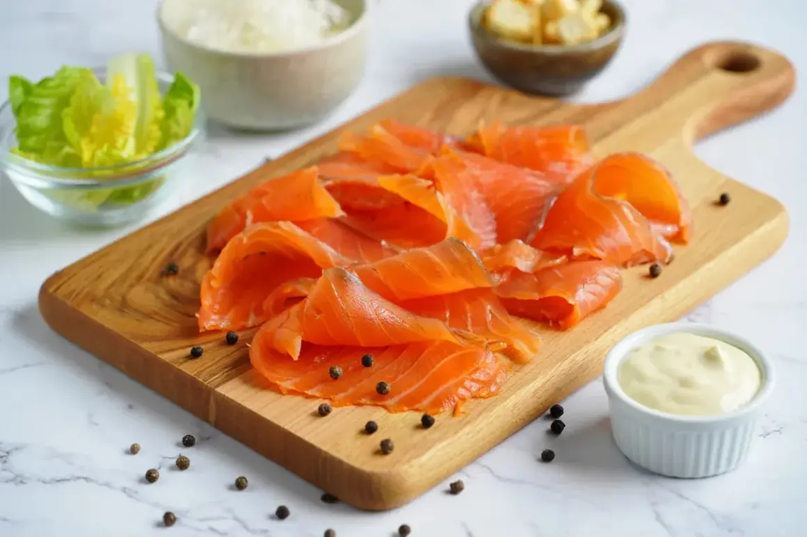 Deliciosa ensalada de salmón lista para preparar. Salmón ahumado en tabla de madera, lechuga, crutones, queso rallado y aderezo.