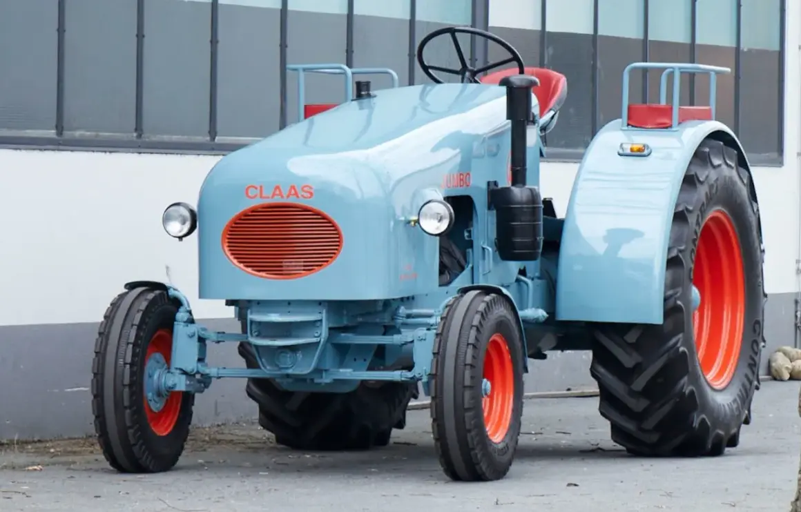 Niebieski ciągnik jednoosiowy Claas Jumbo z pomarańczowymi felgami i grillem.