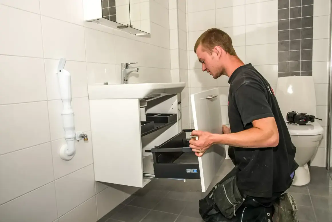 En man installerar en vit kommod i ett kaklat badrum.