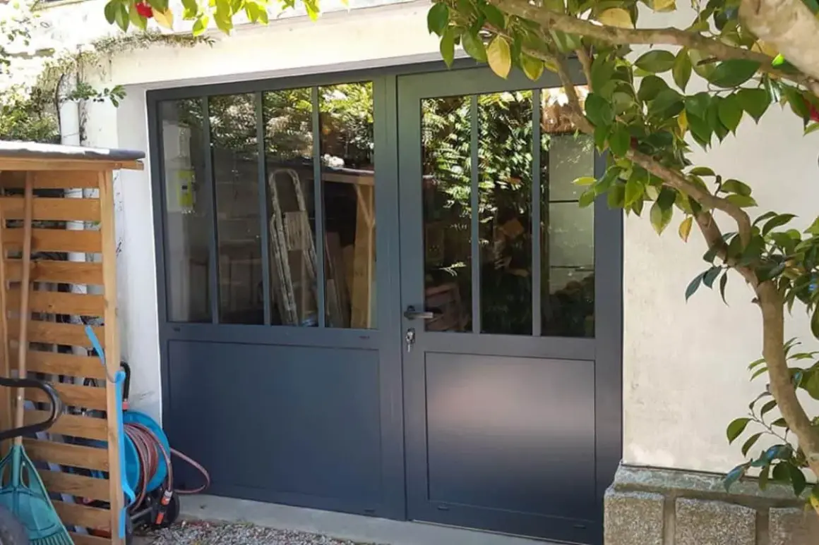 Remplacer porte de garage par fenêtre : une nouvelle entrée lumineuse avec des portes vitrées grises. Des outils de jardin sont rangés à gauche.