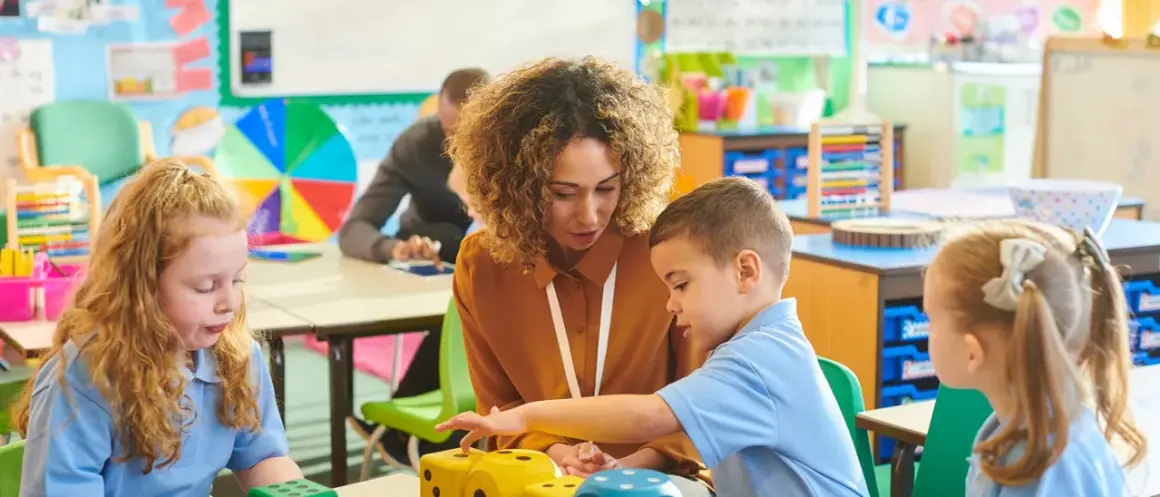 Lehrerin erklärt Kindern in der Schule Mathe mit Würfeln.