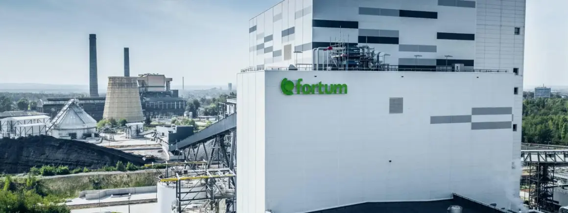 Nowoczesna elektrociepłownia Fortum, gdzie powstaje zielony prąd, z charakterystycznym logo. W tle widać kominy i chłodnie kominowe.