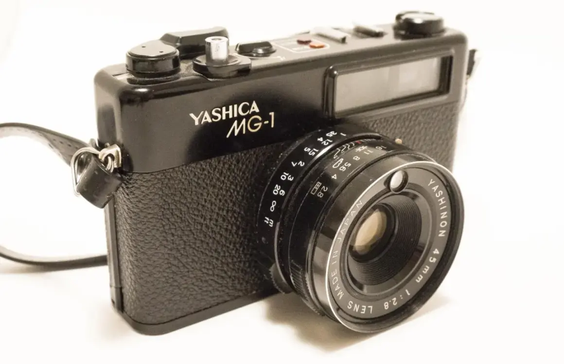 A black Yashica MG-1 camera with a leather strap. The lens reads "YASHINON 45mm 1:2.8".