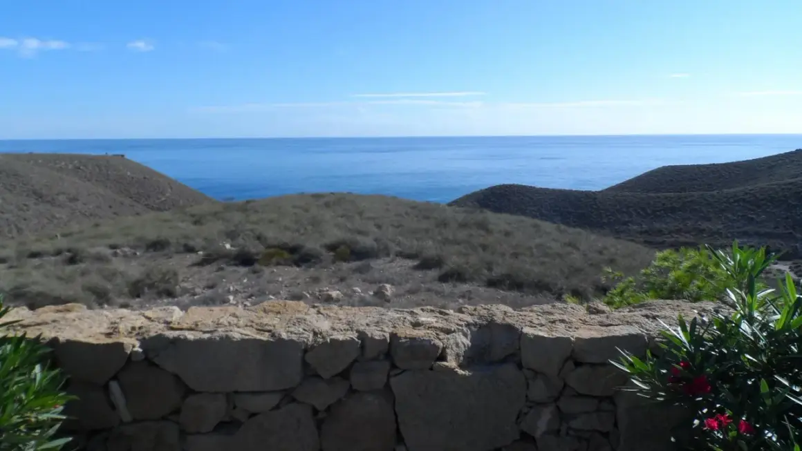 Vista desde una mesa roldan, con el mar azul al fondo y colinas áridas cubiertas de vegetación baja.