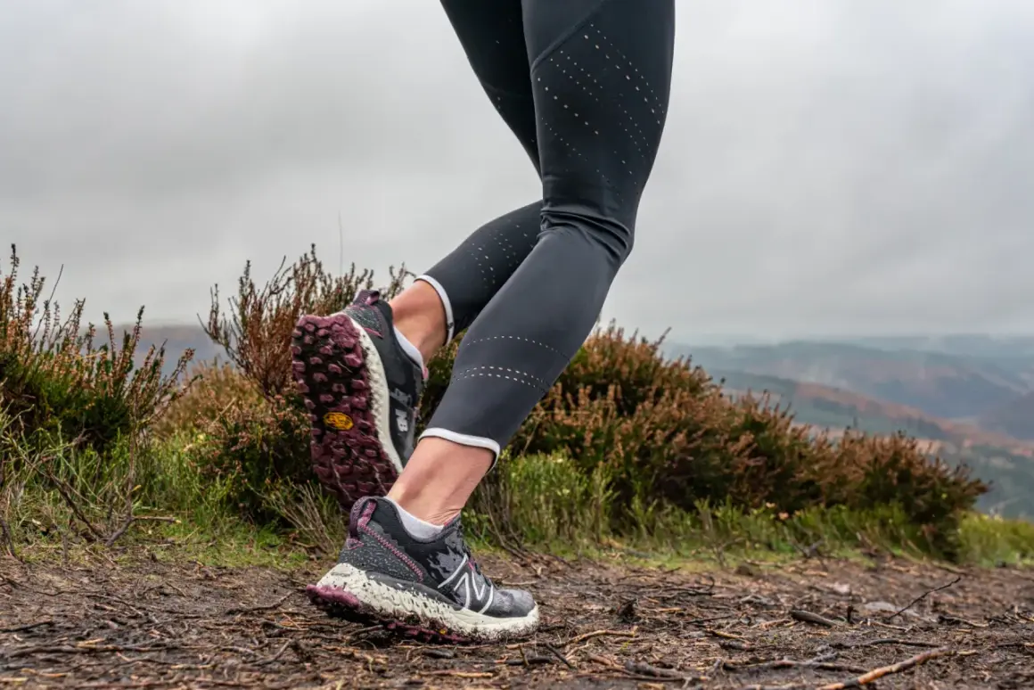 Gambe di una runner su un sentiero fangoso, con erica e colline sullo sfondo. Perfetto per chi vuole iniziare il trail running.